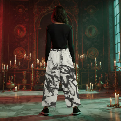 A person stands with their back to the camera in an ornate, candle-lit room, wearing a fitted black long-sleeve top and wide-leg white pants with a bold black abstract brushstroke pattern.