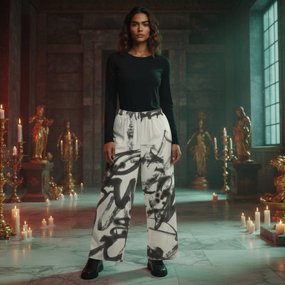 A model stands in a candle-lit hall wearing a black long-sleeve top and high-waisted white wide-leg pants with a bold black abstract brushstroke print. The background features stone walls, classical statues, and numerous lit candles.