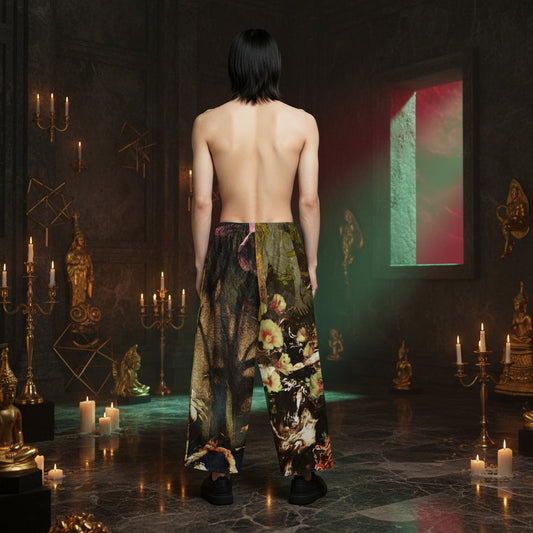 A person stands with their back to the camera in a dark, candle-lit room, wearing loose, wide-leg patterned pants with a split design showing dark floral and scenic imagery on one leg and a lighter floral print on the other.