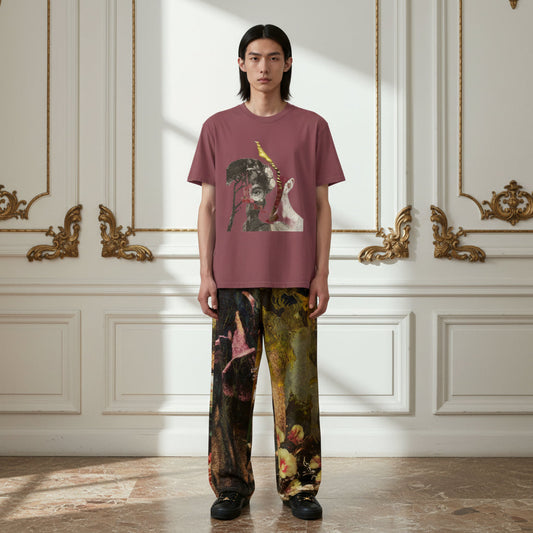 A model stands in a classical European-style room with gold-trimmed white walls, wearing a dusty rose t-shirt with a graphic print of a monkey and a woman, paired with wide-leg pants featuring a complex multicolor classical painting pattern.