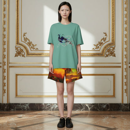 A model stands in a grand, ornate room wearing a sage green t-shirt with a blue peacock graphic and matching multicolor abstract print shorts.
