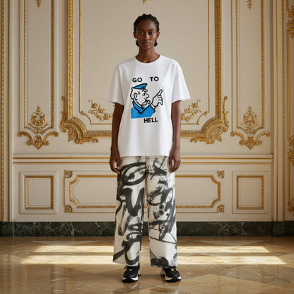 A model stands in a grand, ornate room with gold-trimmed cream walls, wearing a white graphic t-shirt with a blue and black cartoon sailor design and the text 'GO TO HELL', paired with wide-leg white pants featuring a black and gray abstract brushstroke pattern.
