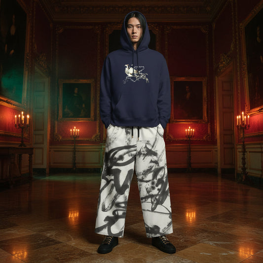 A model stands in a grand, candle-lit historical room wearing a navy blue hoodie with a white graphic on the chest and wide-leg white pants featuring a black ink-blot pattern.