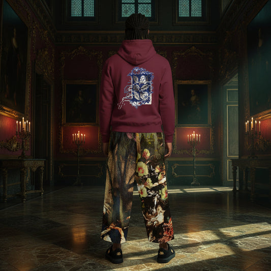 A person standing in a grand, dimly lit historical room, viewed from behind. They are wearing a burgundy hoodie with a large blue and white graphic print on the back, paired with wide-leg, highly detailed floral and scenic print pants and black sandals.